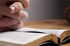 Picture of someones hands folded on a Bible